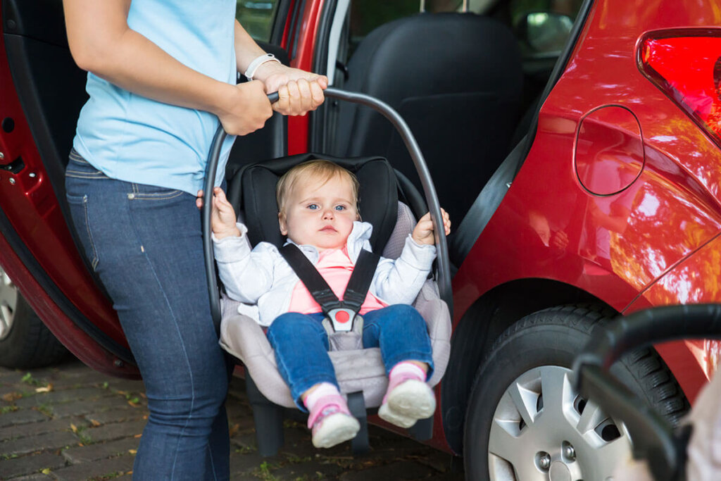 Persoon houdt draagzak met baby vast voor een auto met de deur open