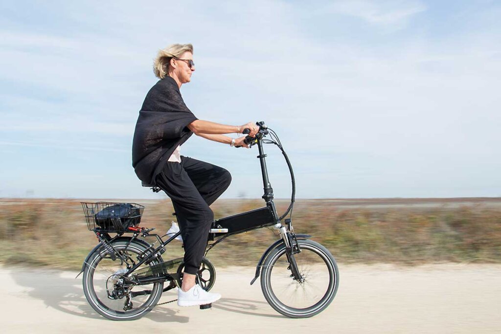 vrouw die vouwfiets op strand rijdt