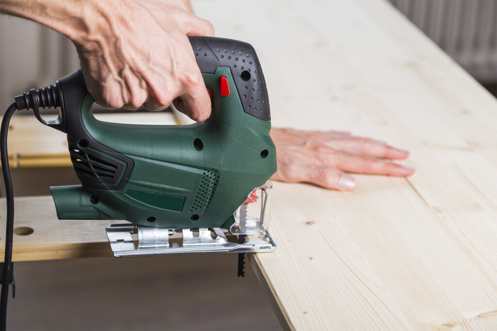 man zaagt met decoupeerzaag houten plank door