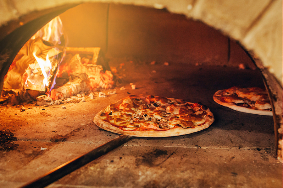 De steenoven voor de zeer populaire, traditionele steenovenpizza wordt verwarmd met hout.