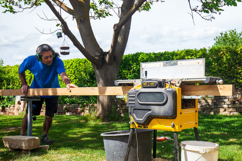 Persoon aan het werk met een schaafmachine in de tuin