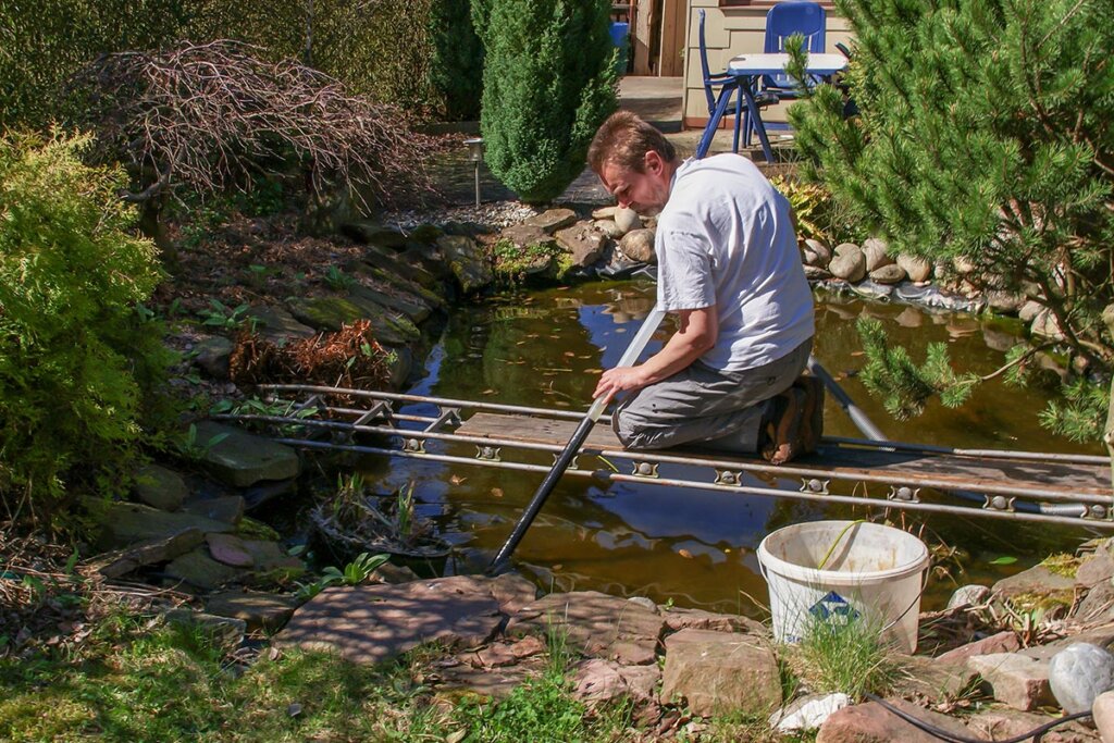 Man maakt tuinvijver schoon met vijvermodderzuiger